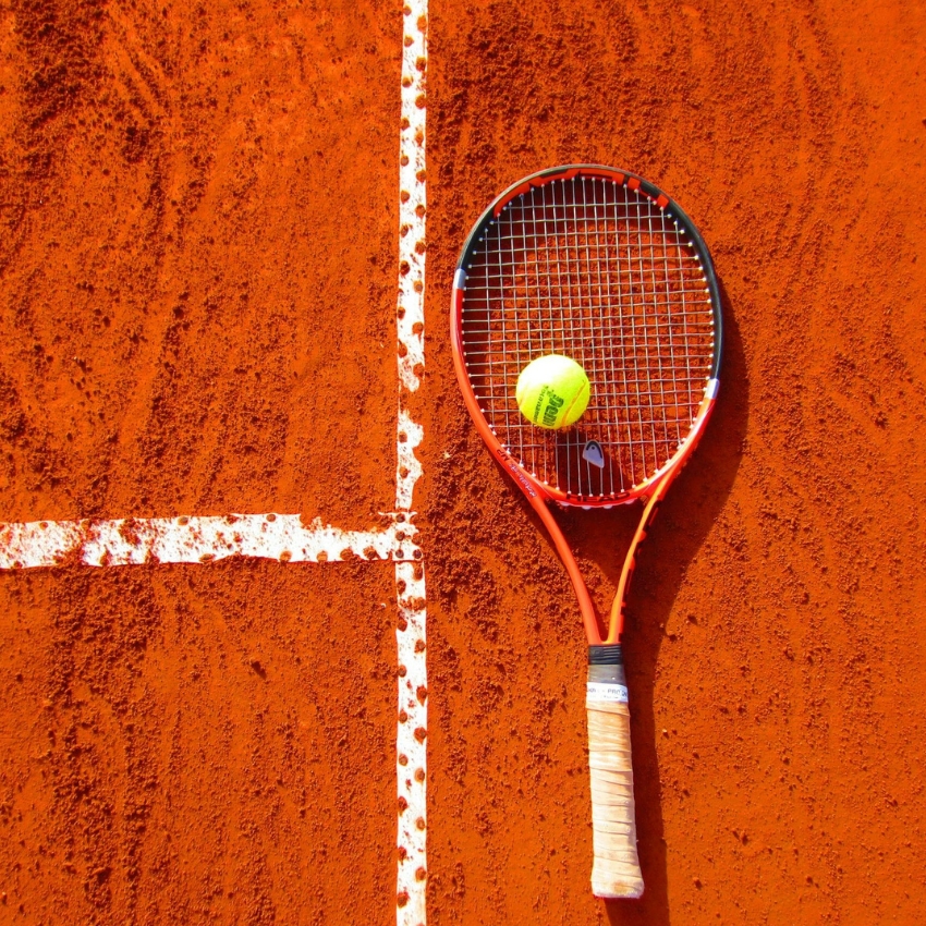 Red tennis racket and yellow tennis ball on a clay tennis court.