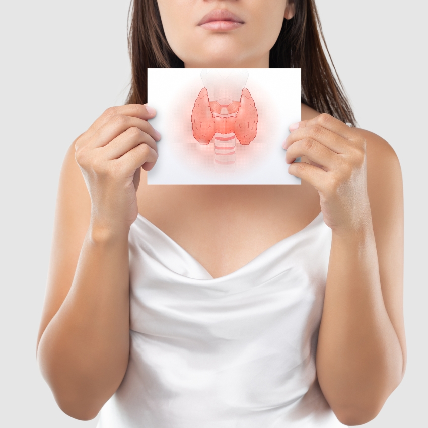 Woman holding a card displaying a diagram of the thyroid gland.