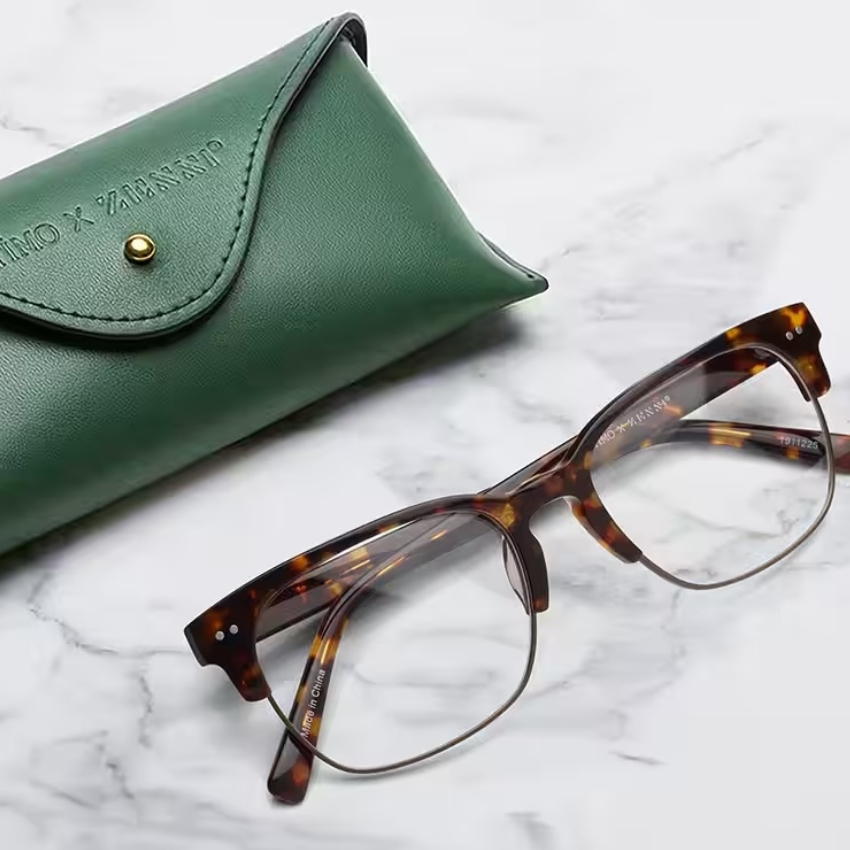 Tortoiseshell eyeglasses alongside a green leather case embossed with "JINS x MASAHIROMARUYAMA."