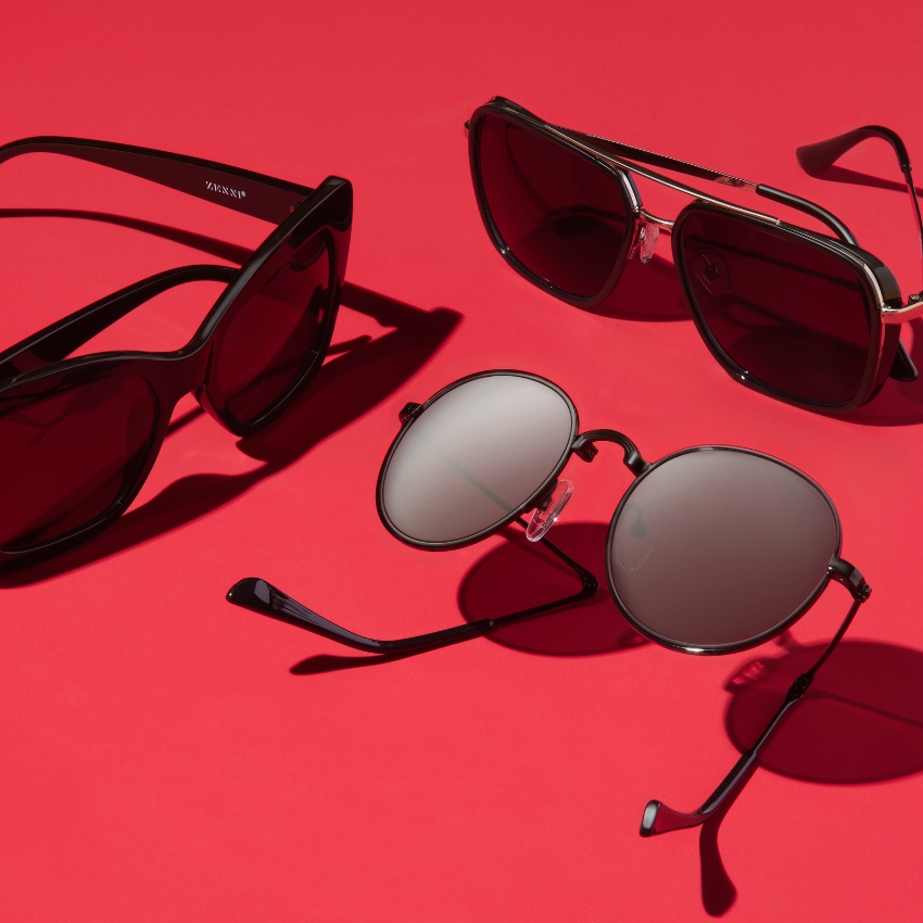 Three pairs of sunglasses on a red background: one cat-eye, one aviator, and one round style. Text on one side: "ZENN".