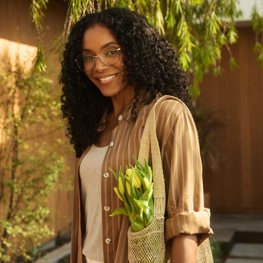 Woman wearing glasses and a striped shirt, holding a mesh bag with yellow tulips.