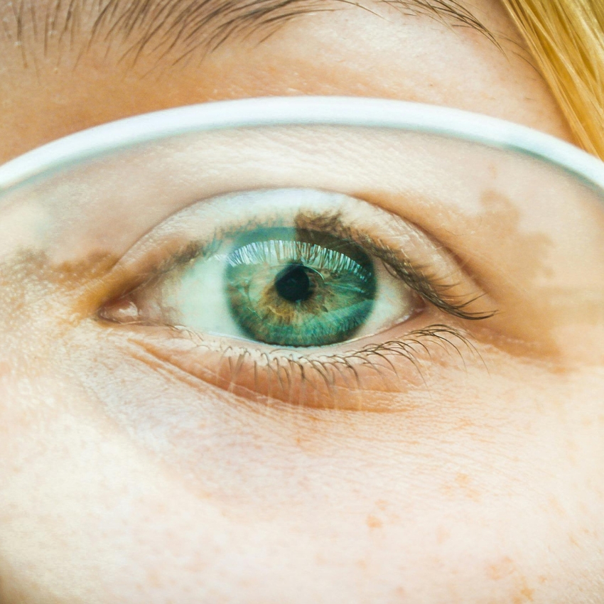 Close-up of a blue-green eye through clear eyeglasses.