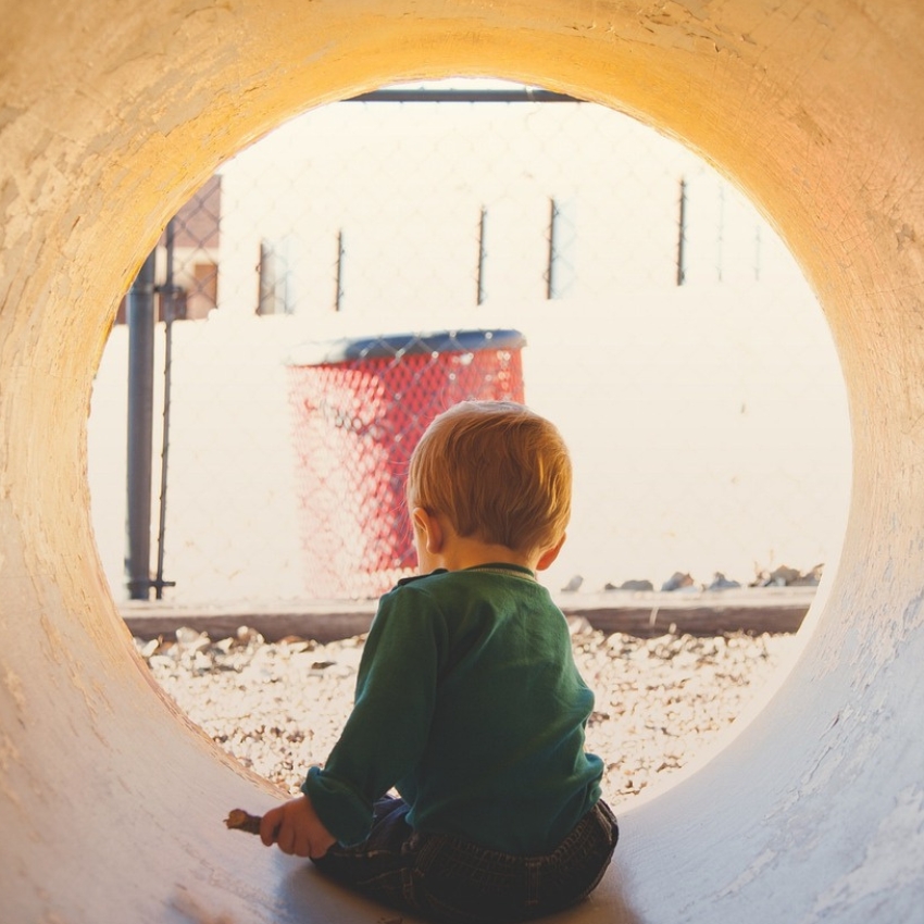 Child in a green shirt sitting in a large concrete pipe opening.