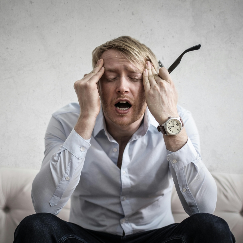 Man holding his head with both hands, wearing a white shirt and a wristwatch.