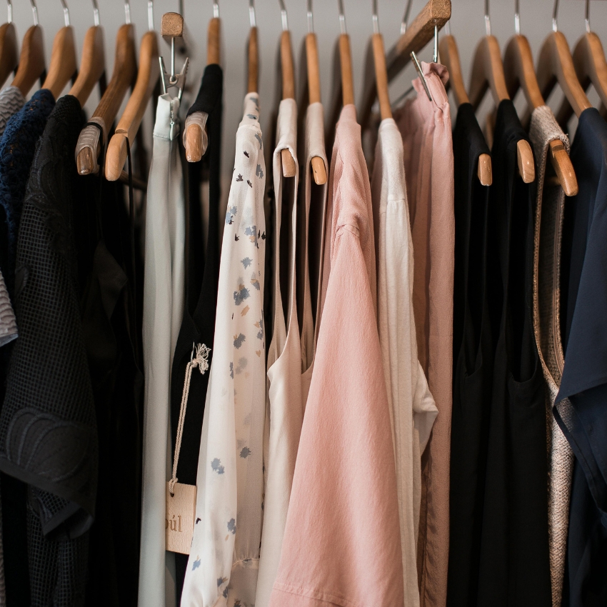 Various blouses and dresses on wooden hangers, including pink, floral, and black items.