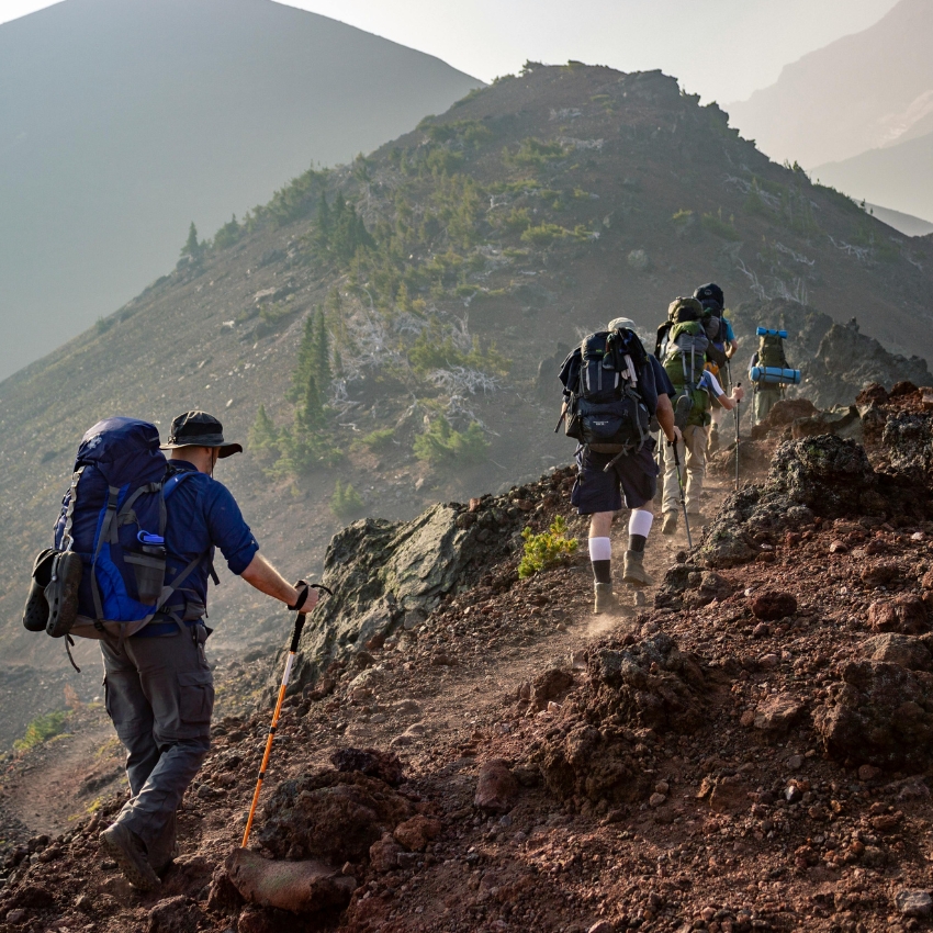 Hikers with large backpacks and trekking poles walking up a rocky incline on a mountain trail.