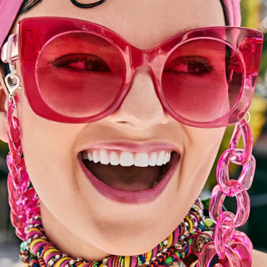 Woman wearing oversized pink sunglasses with pink chain and beaded necklace.