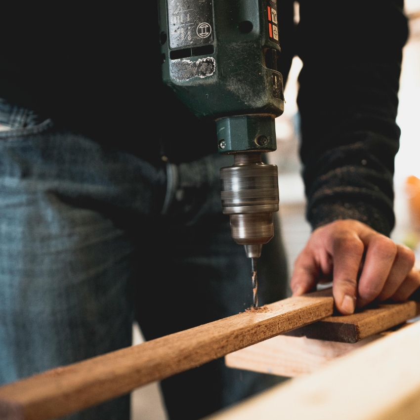 Electric drill boring a hole into a piece of wood held by a person.