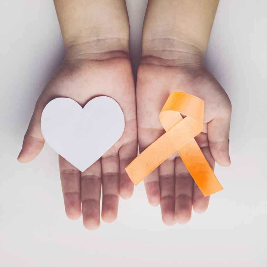 Hands holding a white paper heart and an orange awareness ribbon.