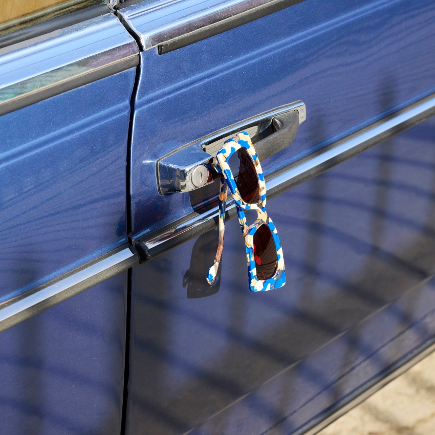 Blue and white patterned sunglasses hanging on a blue car door handle.