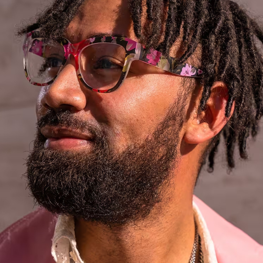 Man wearing colorful floral-patterned glasses with a clear frame, featuring shades of pink, red, and green.