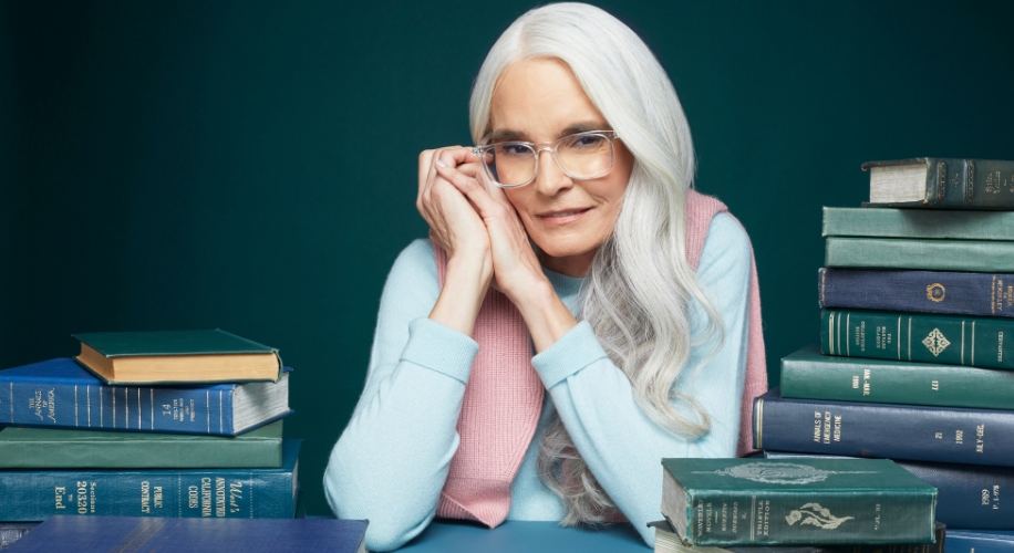 Woman wearing reading glasses next to a pile of books