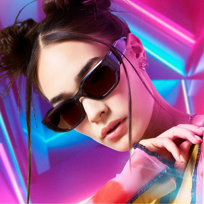 Woman wearing dark rectangular sunglasses with a black frame against a colorful neon background.