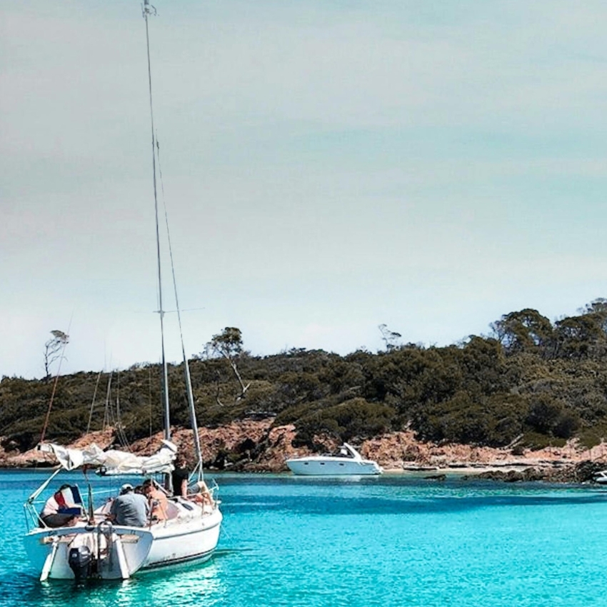 A small sailboat with people onboard floating on clear, turquoise water.