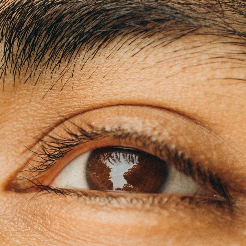 Close-up of a human eye with trees and sky reflected in the pupil.