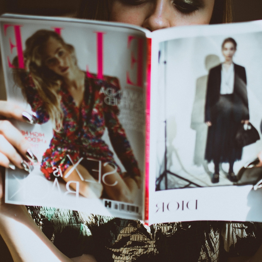 Person reading open Elle magazine. Cover features a woman in a colorful outfit. Page reads "DIOR".