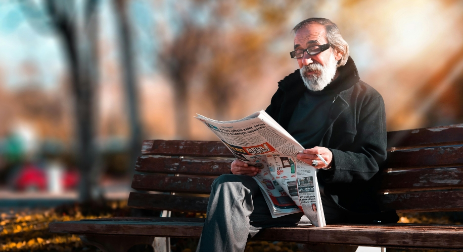 Man sitting on bench reading newspaper