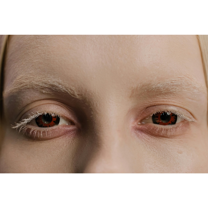 Red and black colored contact lenses in the eyes of a person with blonde eyebrows and eyelashes.