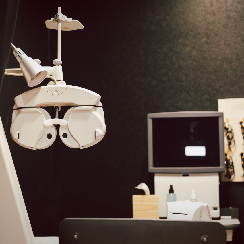 Phoropter for eye exams with adjustable lenses and knobs, illuminated by an overhead lamp.