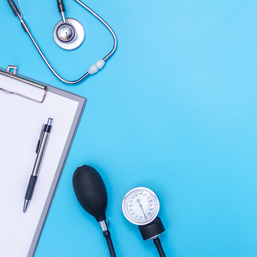 Stethoscope, blood pressure monitor, clipboard with pen on blue background.