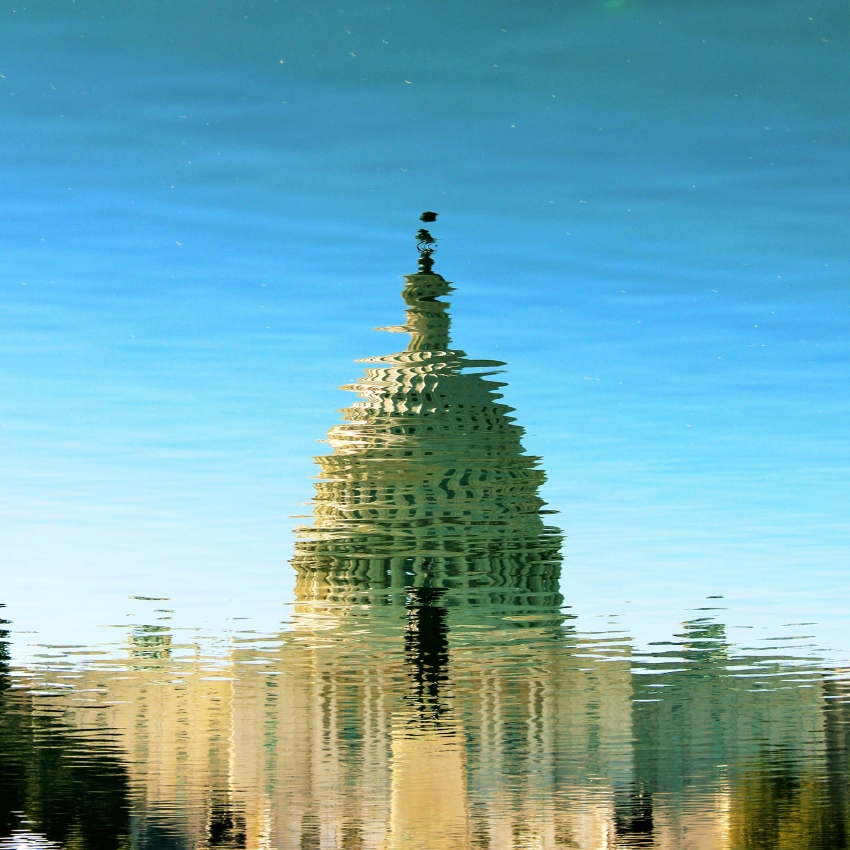 Reflection of a domed building with intricate details on calm water under a clear blue sky.