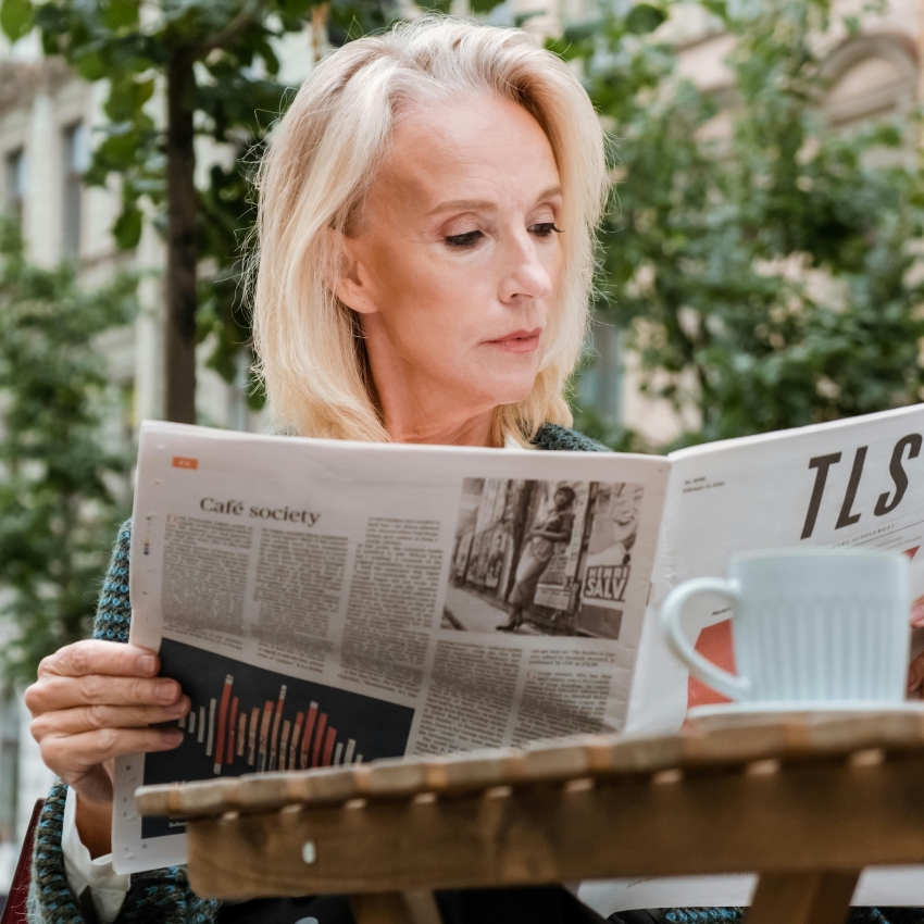 Woman reading a newspaper with a visible article titled "Café society."