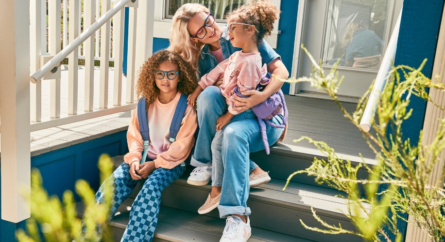 A woman and two kids wearing stylish glasses are sitting on outdoor steps, smiling and laughing.