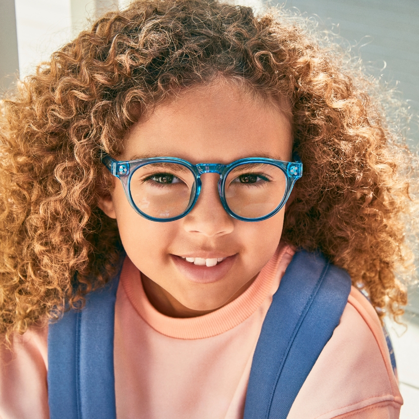 Child wearing blue round eyeglasses and a pink top with blue straps.