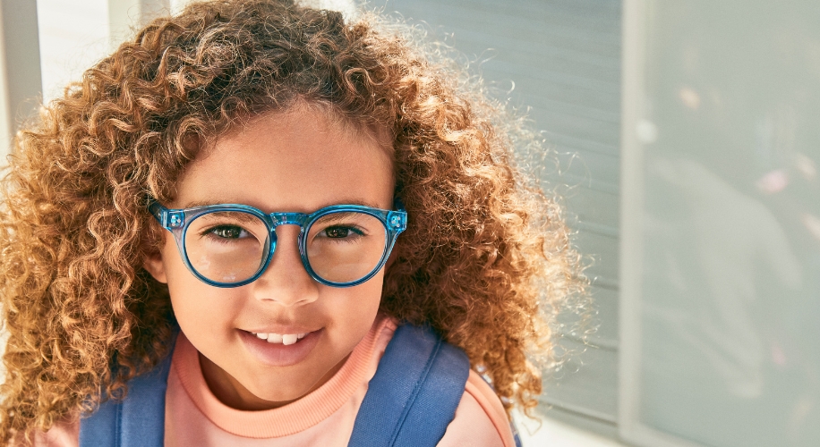 Child wearing blue eyeglasses with a clear frame and a pink sweater.