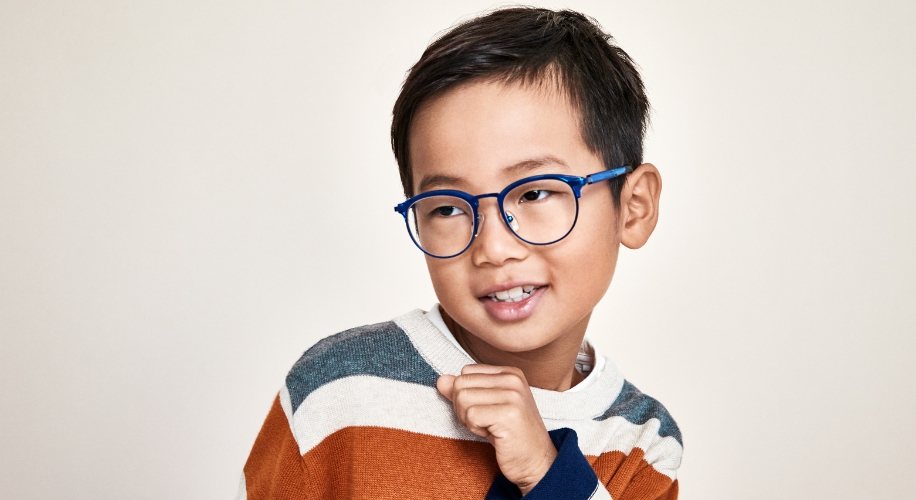 Child wearing blue round glasses and a striped sweater with grey, white, rust, and blue colors.