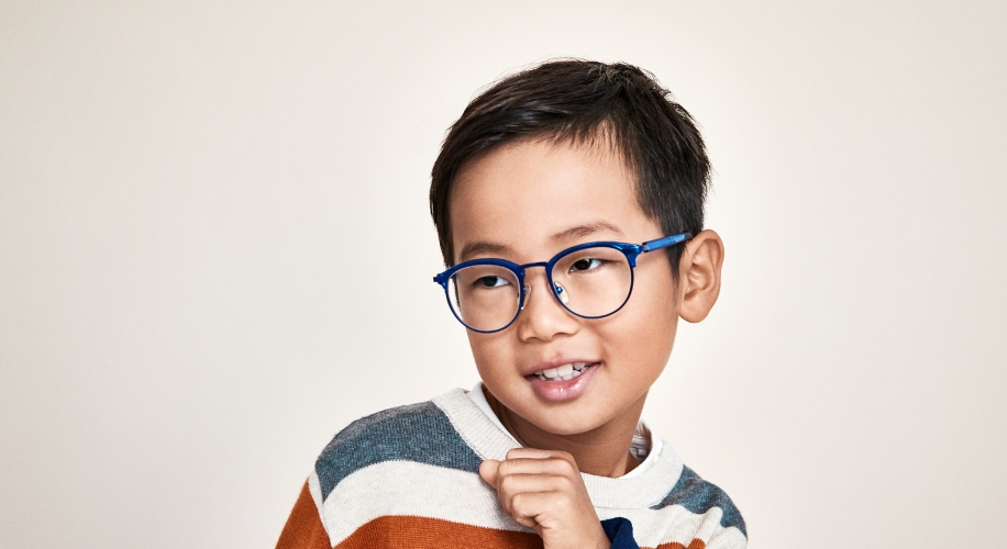 Child wearing blue glasses and a striped sweater with a beige background.