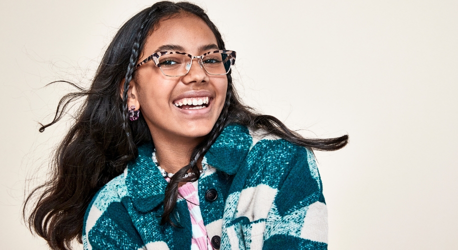 Woman wearing patterned eyeglasses and smiling while dressed in a teal and white plaid jacket.