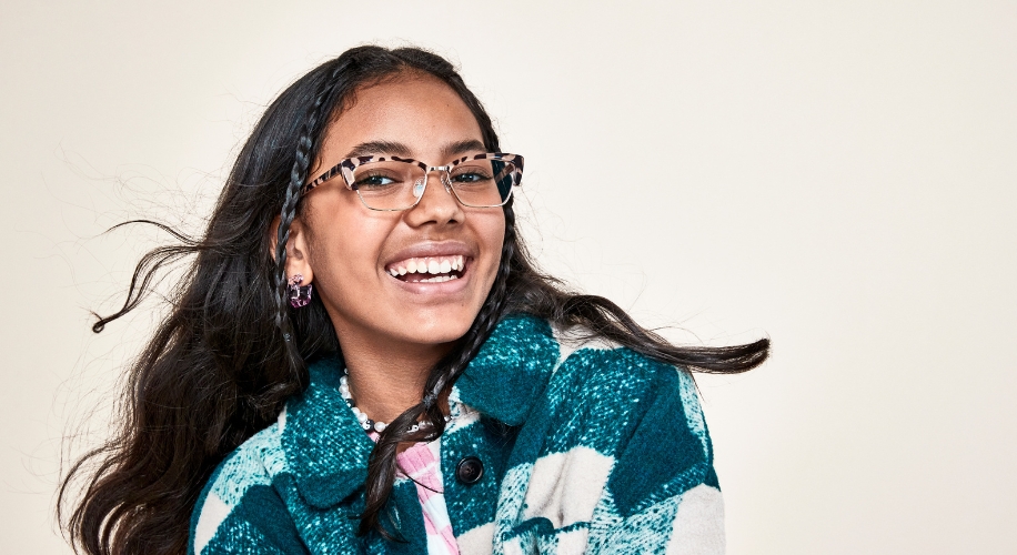 Girl wearing stylish eyeglasses and a blue and white checkered jacket, smiling.