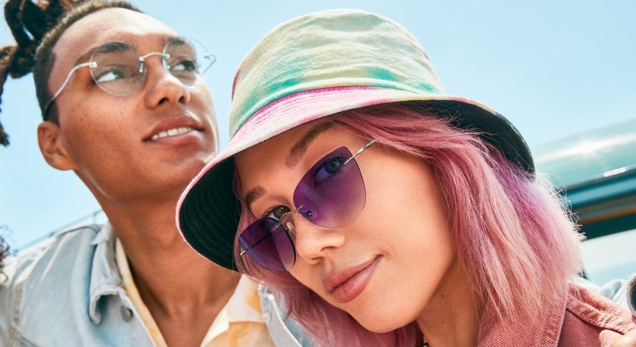 Two individuals wearing stylish sunglasses, one with a pastel tie-dye bucket hat and pink-tinted lenses.