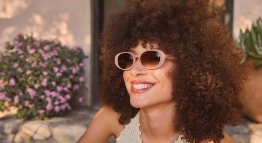 Smiling person wearing stylish, round pink sunglasses.