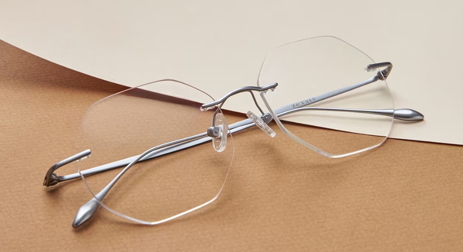 Rimless eyeglasses with silver temples on a brown and beige surface.