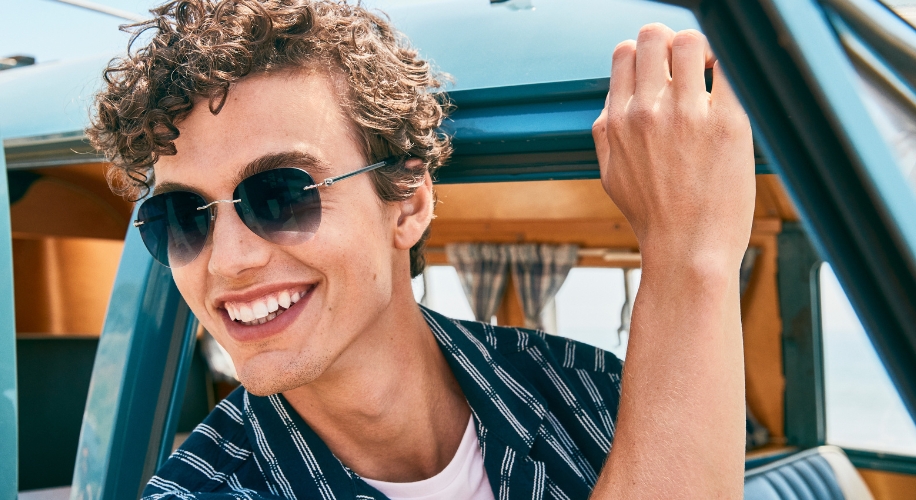 Man wearing round black sunglasses and smiling in a vehicle.