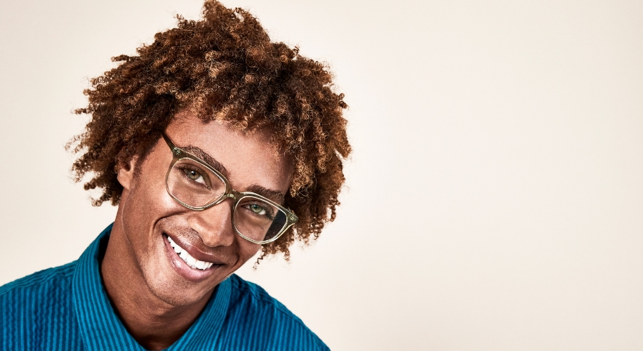 Man wearing transparent green eyeglasses and a blue shirt, smiling.