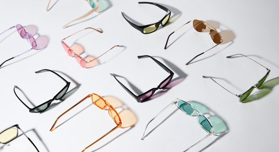 Assorted sunglasses with various colored lenses: purple, pink, yellow, brown, green, and blue.