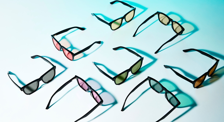 Various sunglasses with black frames and different colored lenses on a light surface.