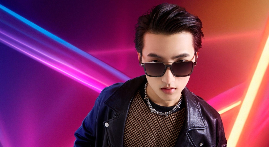 Person wearing black sunglasses, a black fishnet shirt, and a black leather jacket against a neon-lit background.