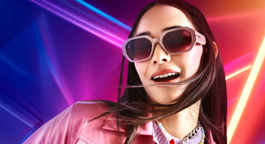 Woman wearing oversized pink sunglasses against colorful, neon-lit background.