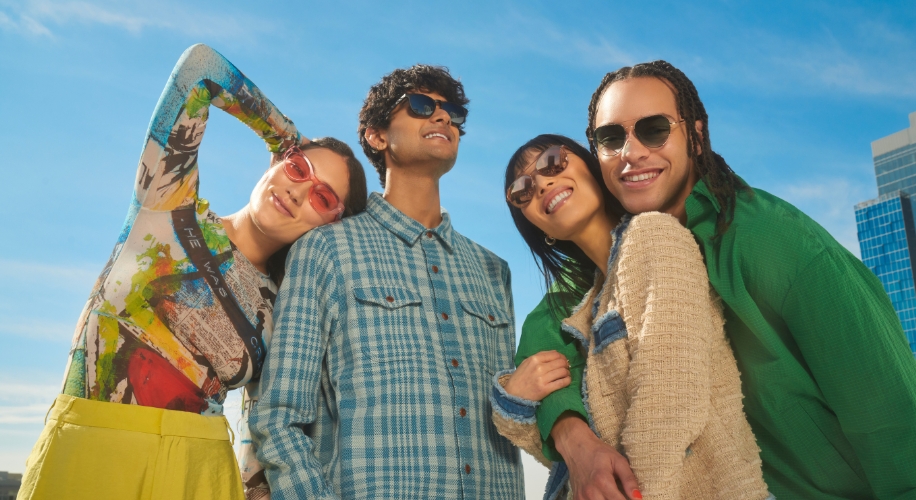 Four people wearing colorful, fashionable sunglasses smiling under a clear blue sky.