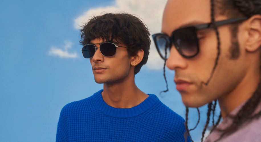 Two individuals wearing stylish sunglasses, one in a blue sweater and the other with braids.