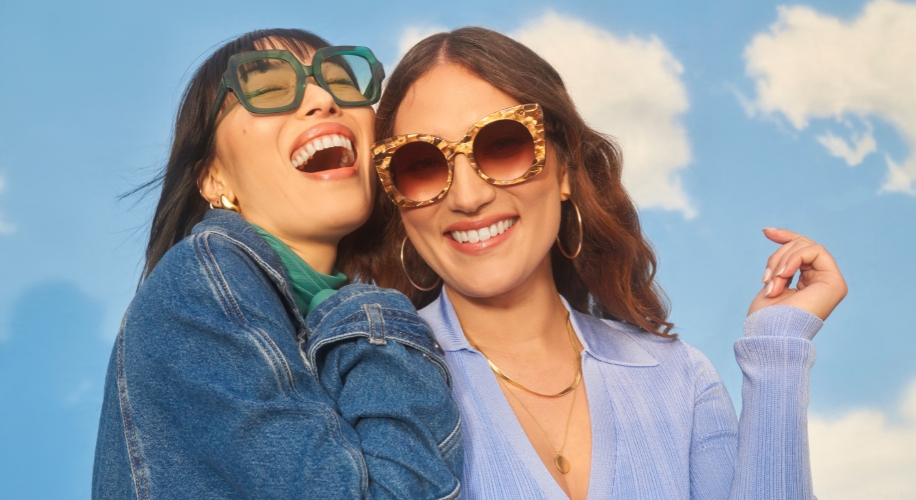 Two women smiling, showcasing oversized sunglasses, one in green frames, the other in tortoiseshell frames.