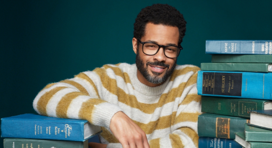 Man in striped sweater with several medical textbooks. Titles include &quot;Surgery&quot; and &quot;Advanced Surgery&quot;.