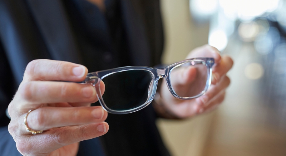 Hands holding transparent eyeglasses with rectangular frames.