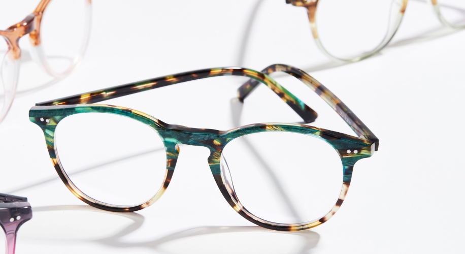 Green and tortoiseshell patterned eyeglasses with round frames, shown with other glasses in the background.