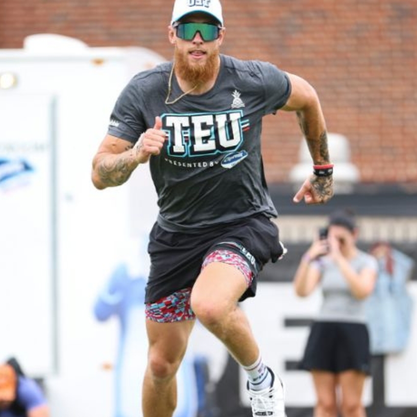 Man running while wearing grey shirt with "TEU," "PRESENTED BY," and "OB", and a white cap with "OBF".