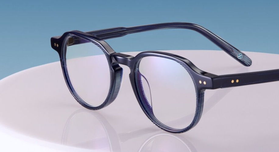 Black-rimmed eyeglasses with round lenses and gold rivets on the corners, reflecting a blue hue.